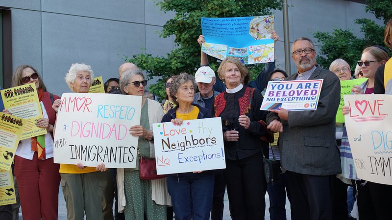Faith leaders and community members holding signs reading “Love Thy Neighbors, No Exceptions,” “Amor, Respeto y Dignidad para Inmigrantes,” and “You Are Beloved, No Exceptions”