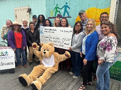 Pacifica Resource Center staff and the Pacificans Care bear mascot holding a large Pacificans Care check